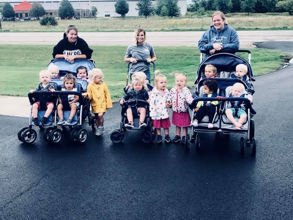 Three people pushing multiple children in strollers