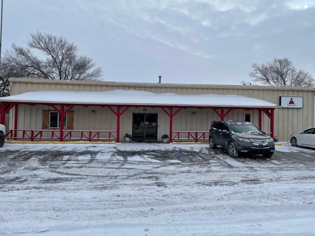 Snow-covered building with red porch railings and cars in a snowy parking lot