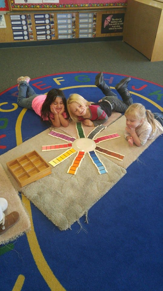 Three children lying on a rug looking at color swatches arranged in a circle