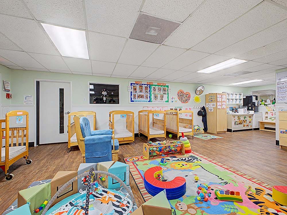 A childcare room with cribs, playmats, and toys