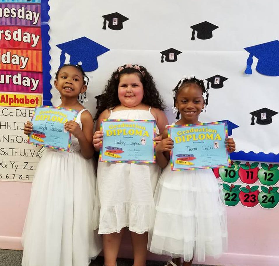 Three children in white dresses holding diplomas