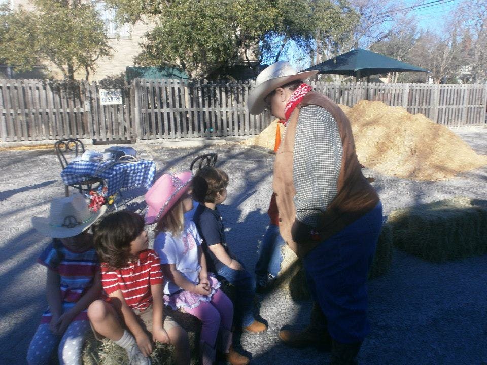 Person in cowboy hat and vest talking to children
