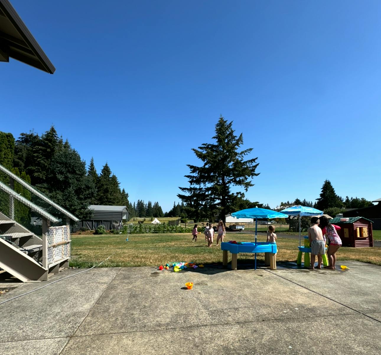Children playing outdoors near a blue umbrella and small playhouse