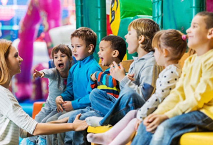 Adult speaking to a group of children sitting in a row