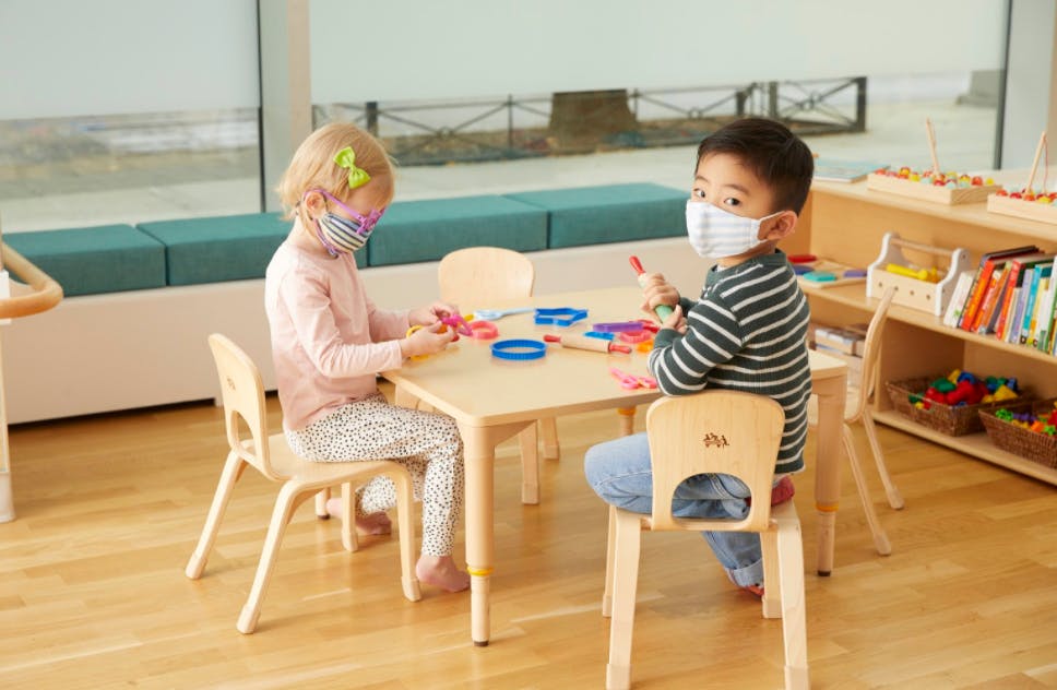 Two children wearing masks sitting at a table in a classroom