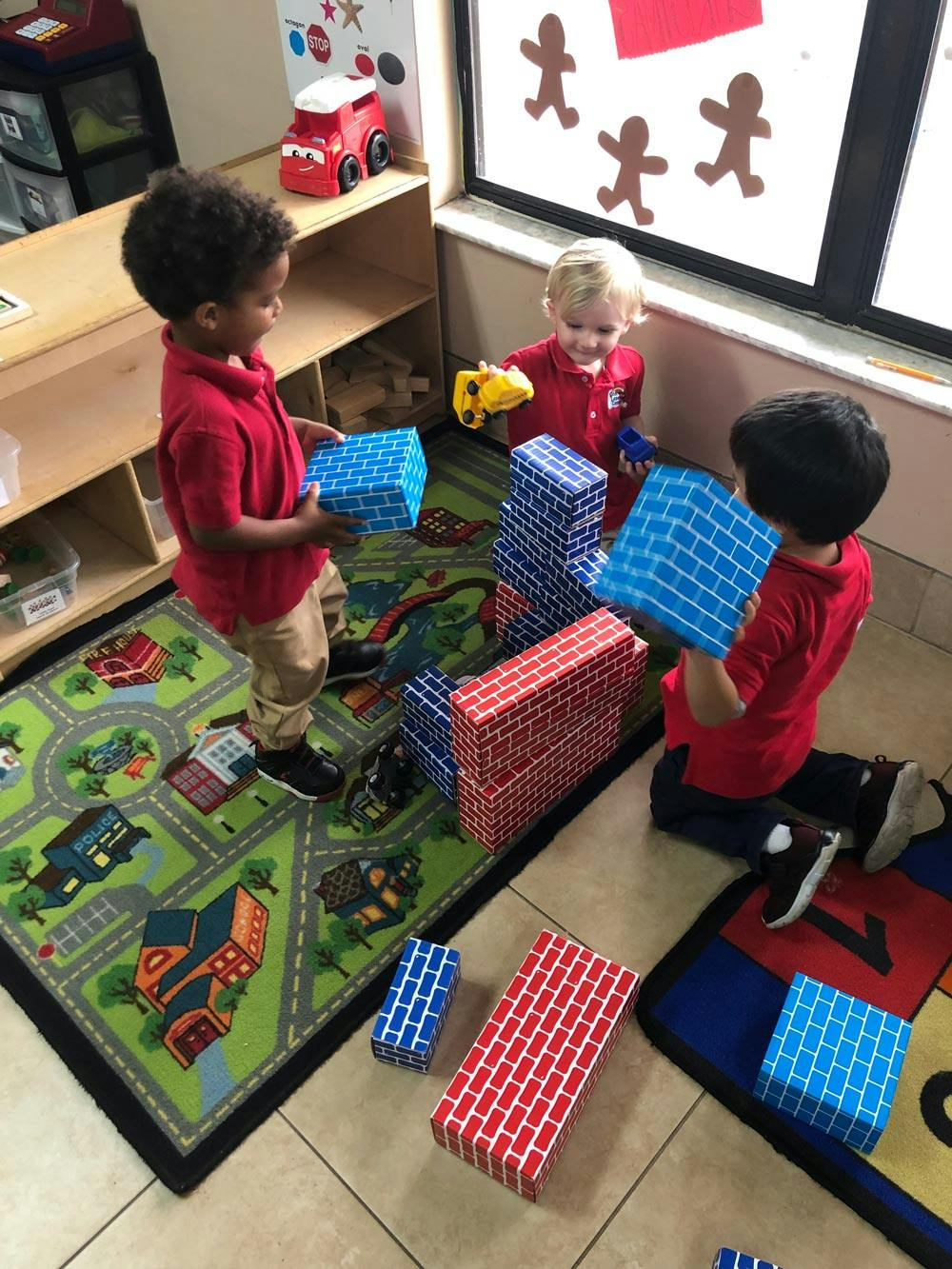 Three children playing with large building blocks in a classroom