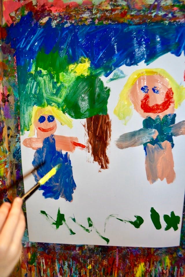 Child's hand painting a picture of two people and a tree
