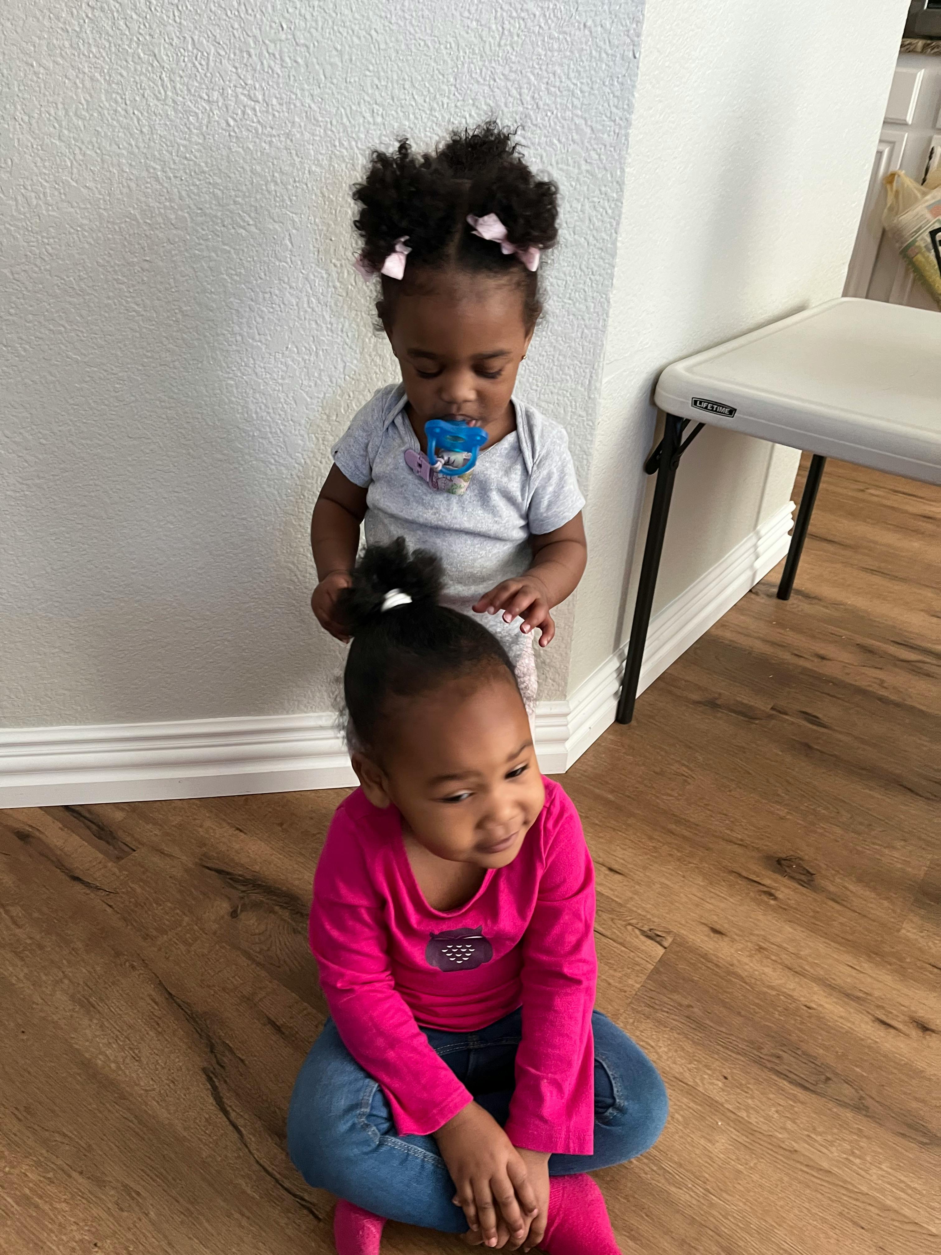 Two children, one sitting on the floor and one standing behind
