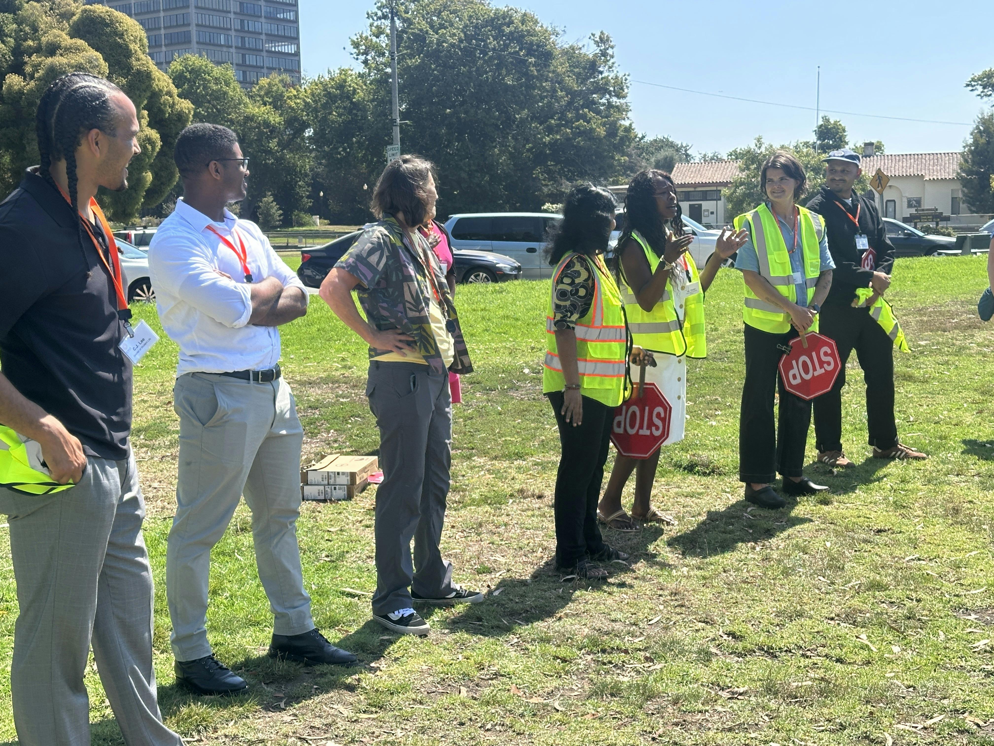 Group of people in outdoor setting, some wearing safety vests and holding stop signs
