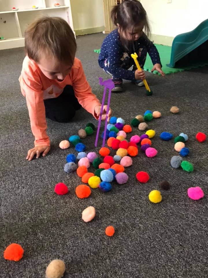 Two children playing on the floor with colorful pom-poms and toys