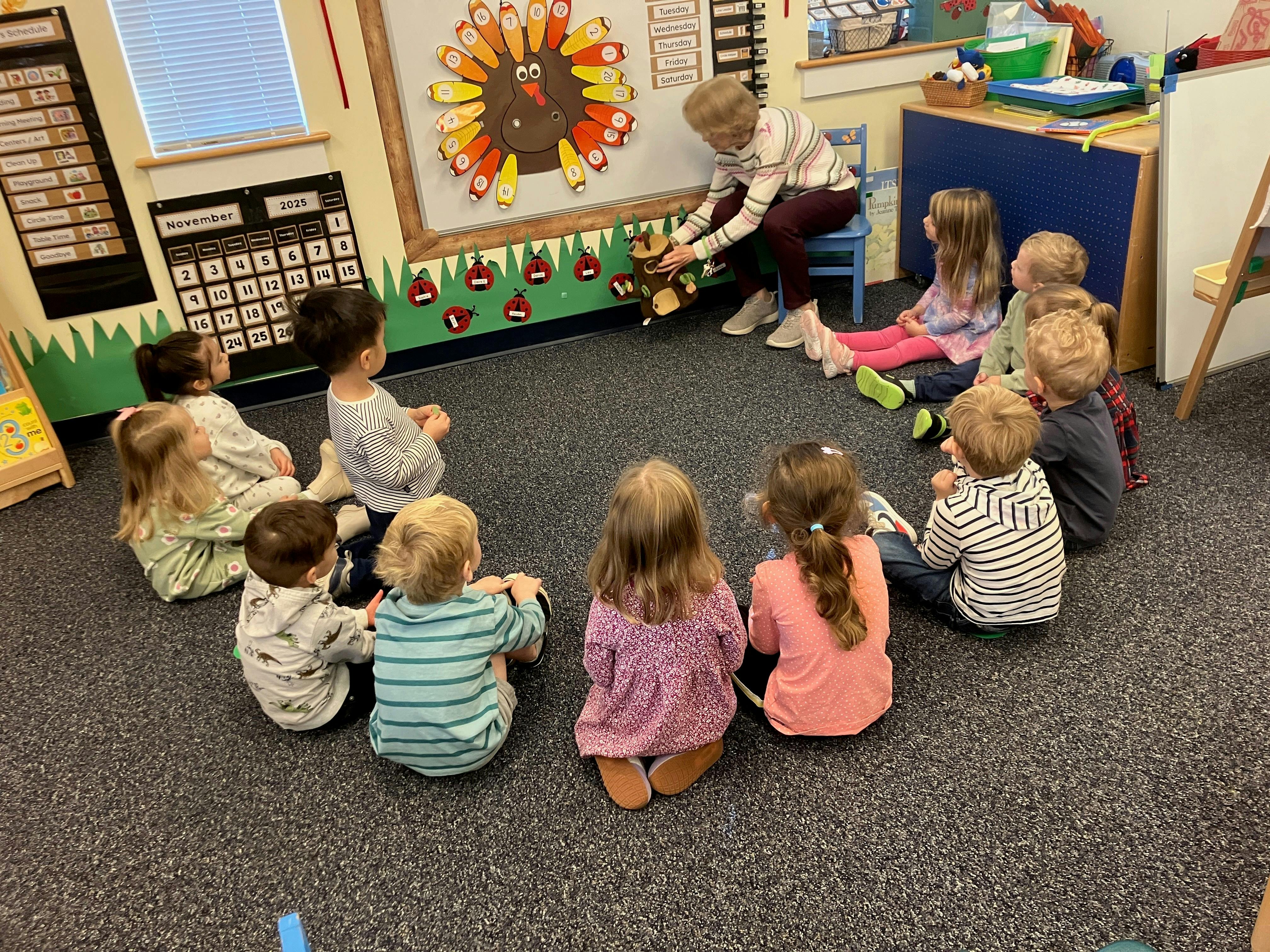 A person sitting on a chair presenting to a group of children seated on a carpet