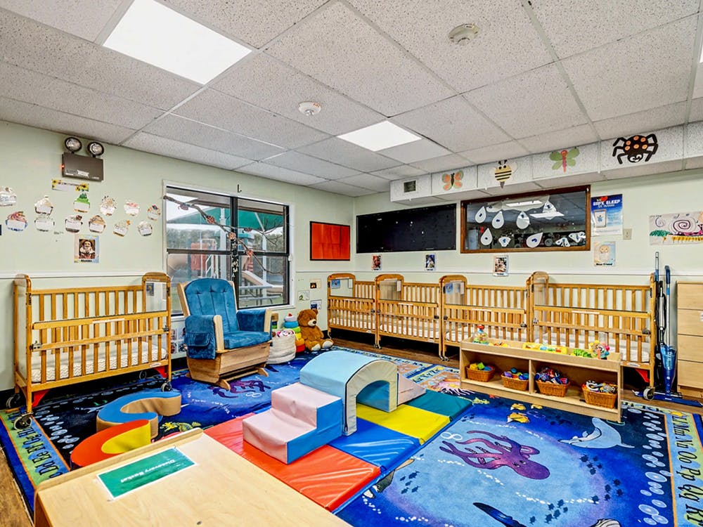 Classroom for babies with cribs, playmats, and a rocking chair