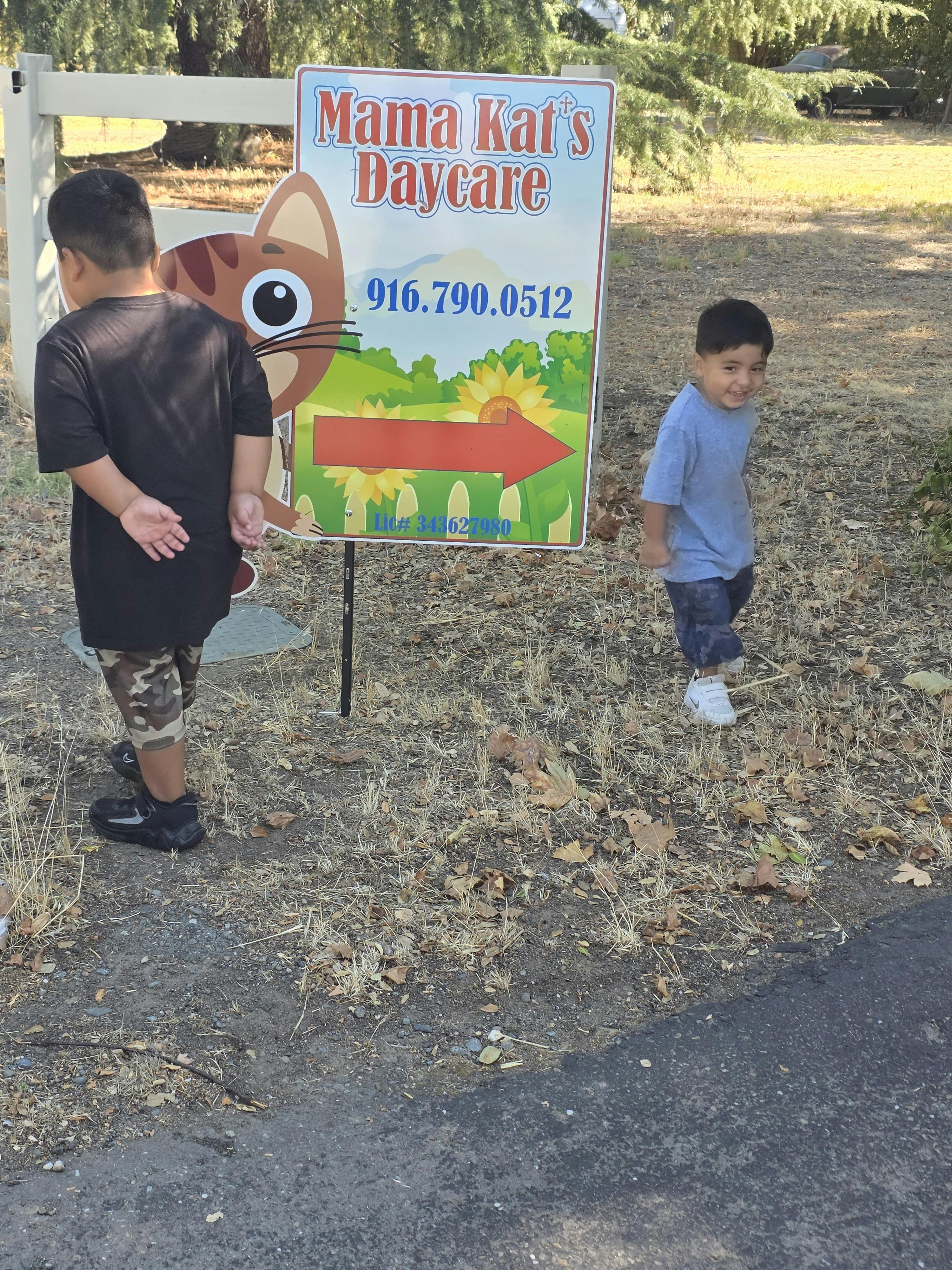 Two children standing by a sign for Mama Kat's Daycare