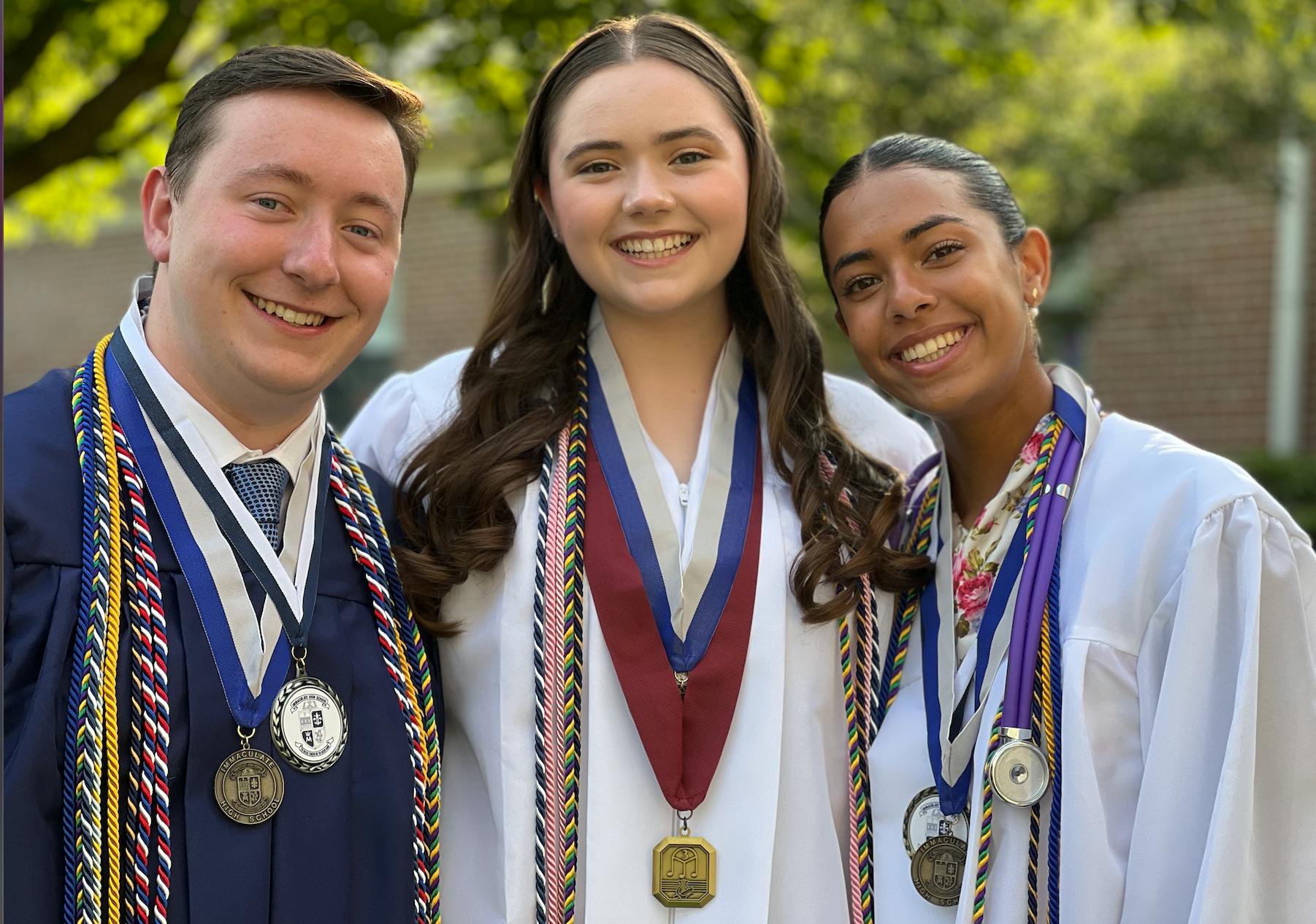 Three people wearing graduation robes and stoles standing together outdoors