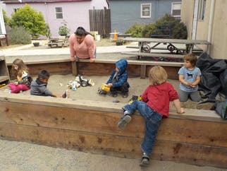 Adult supervising children playing in a sandbox