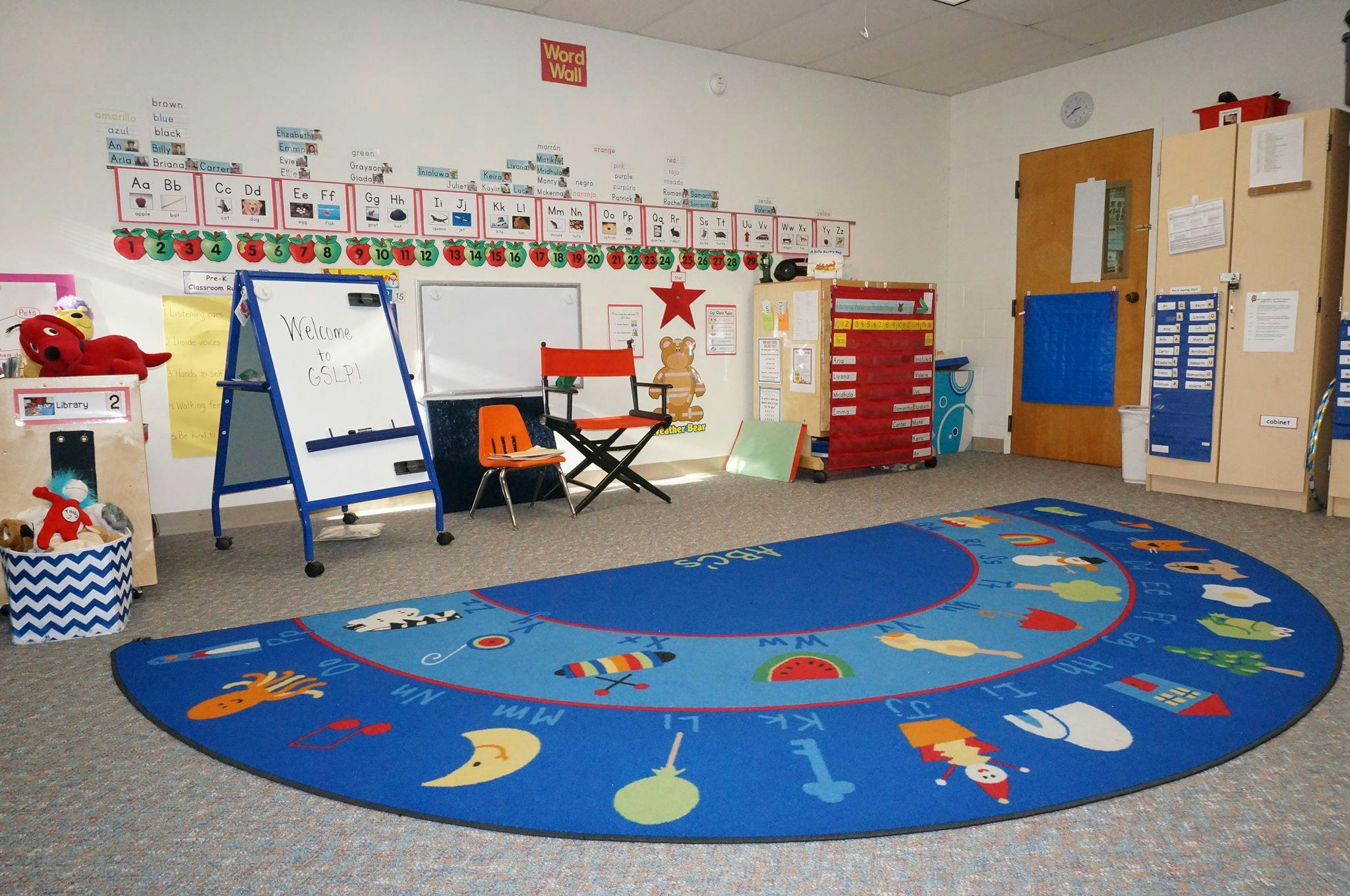 Classroom with a blue semicircular rug, whiteboard, and chairs