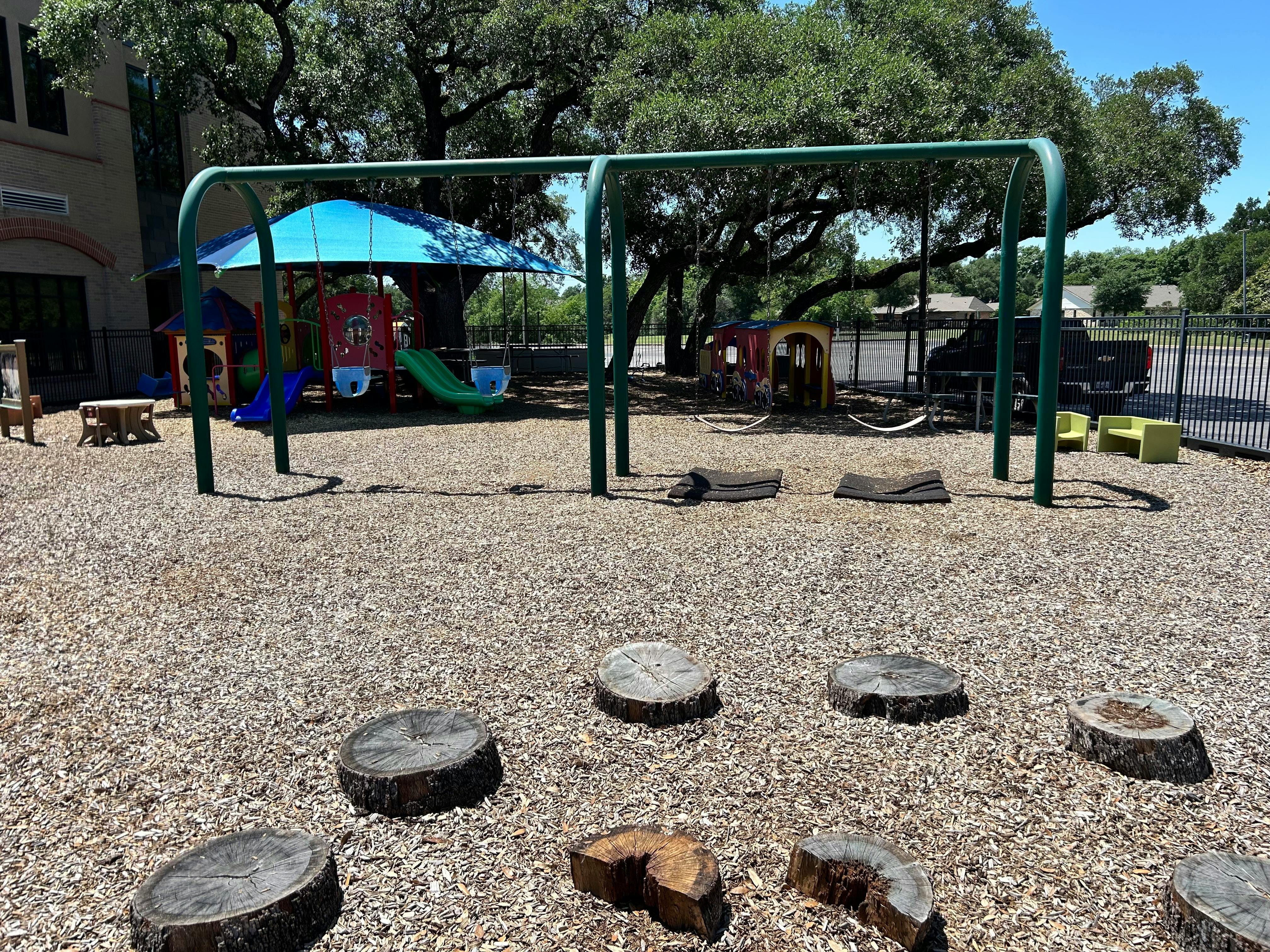Playground with swings, slides, and tree stumps on wood chips