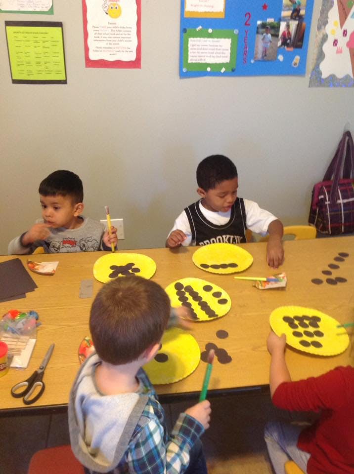 Children at a table doing a craft with yellow paper plates and brown circles