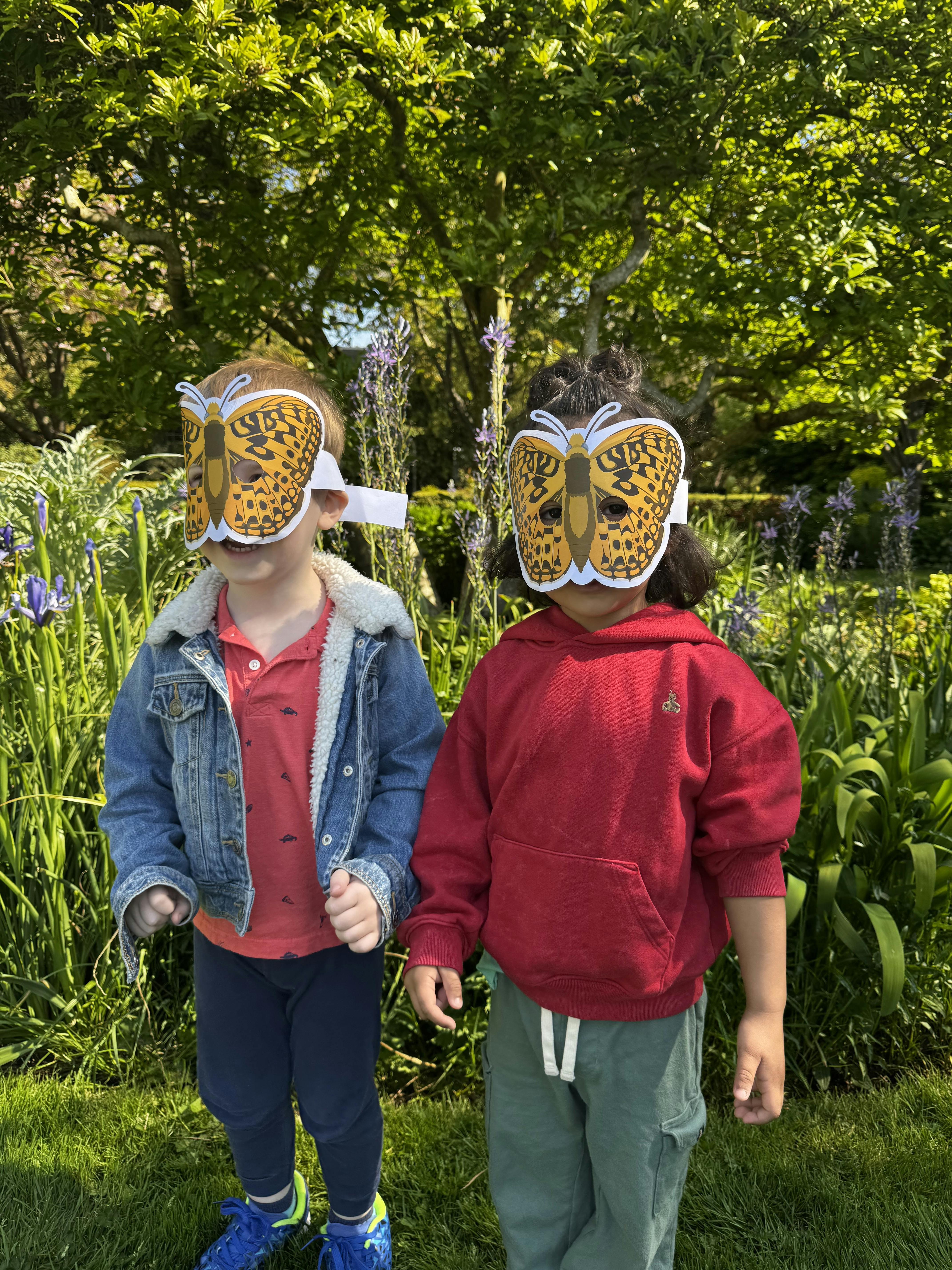 Two children wearing butterfly masks outdoors