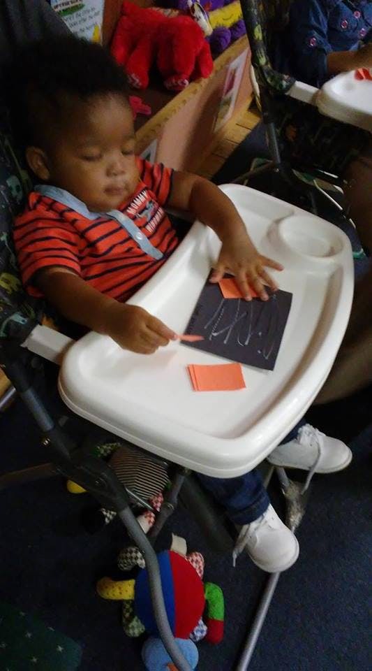 Child in a high chair playing with paper cutouts and glue