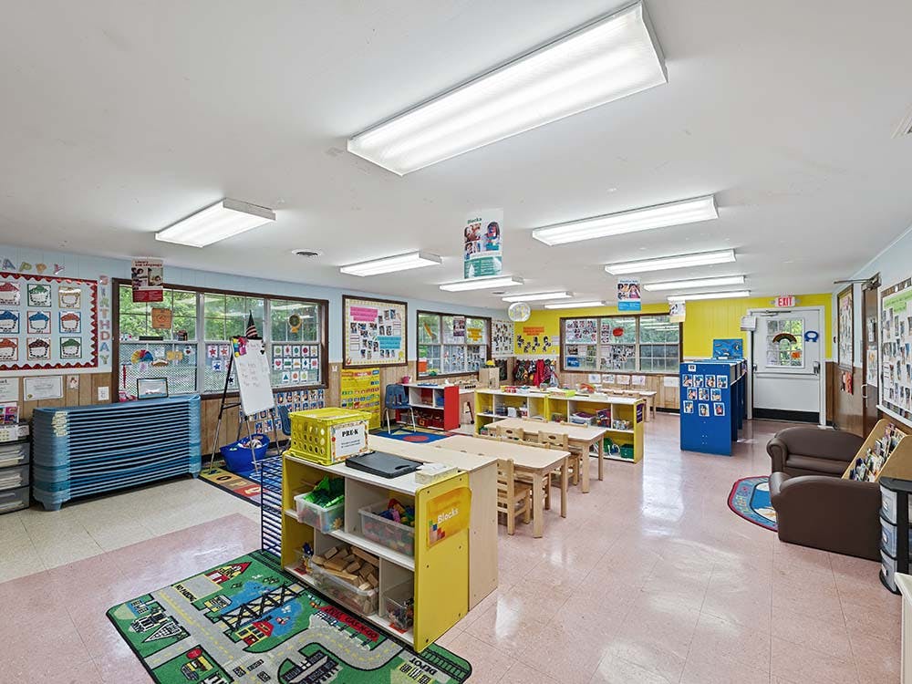 Classroom with small tables and chairs, shelves with toys, and posters on the walls