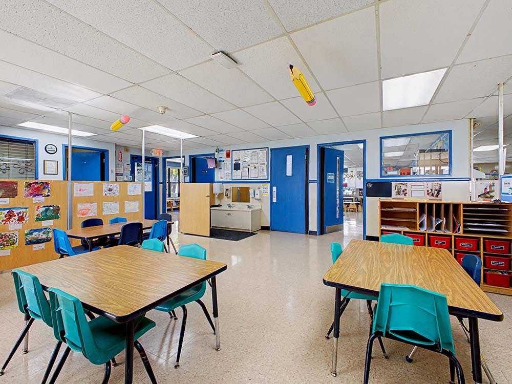 Empty classroom with small tables and chairs, artwork on walls, blue doors