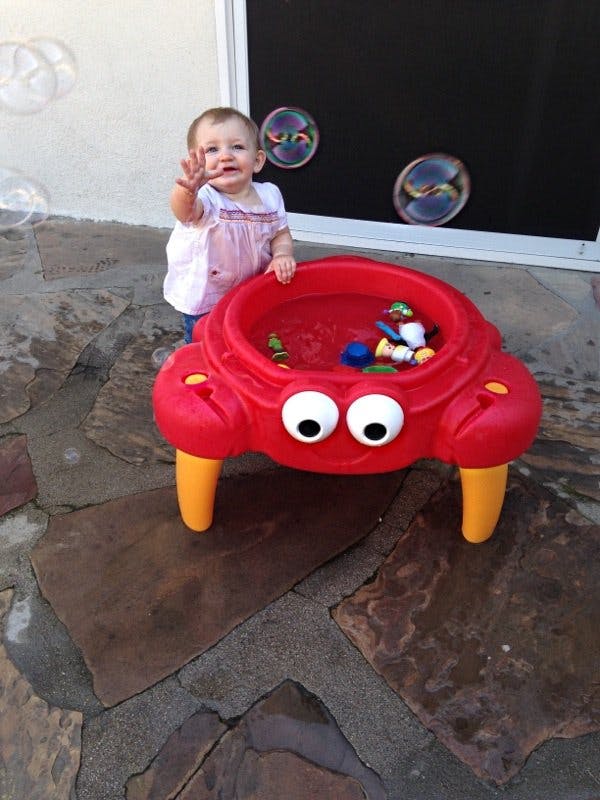 Child standing next to a red crab-shaped water table with bubbles floating around
