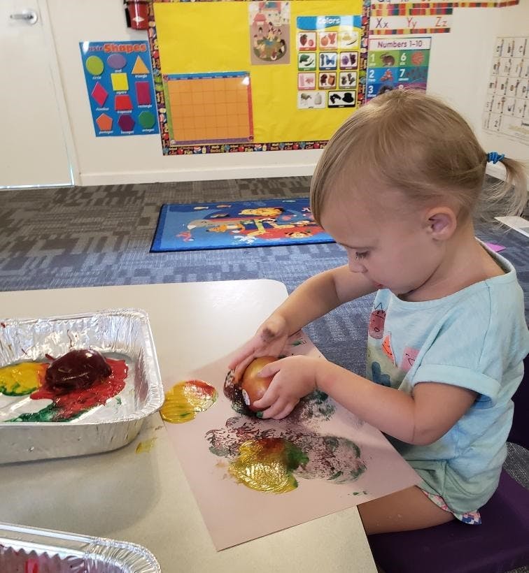 Child making art with paint and an apple in a classroom