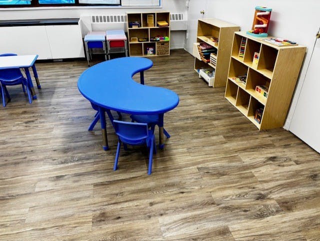Classroom with blue tables and chairs, and wooden shelves