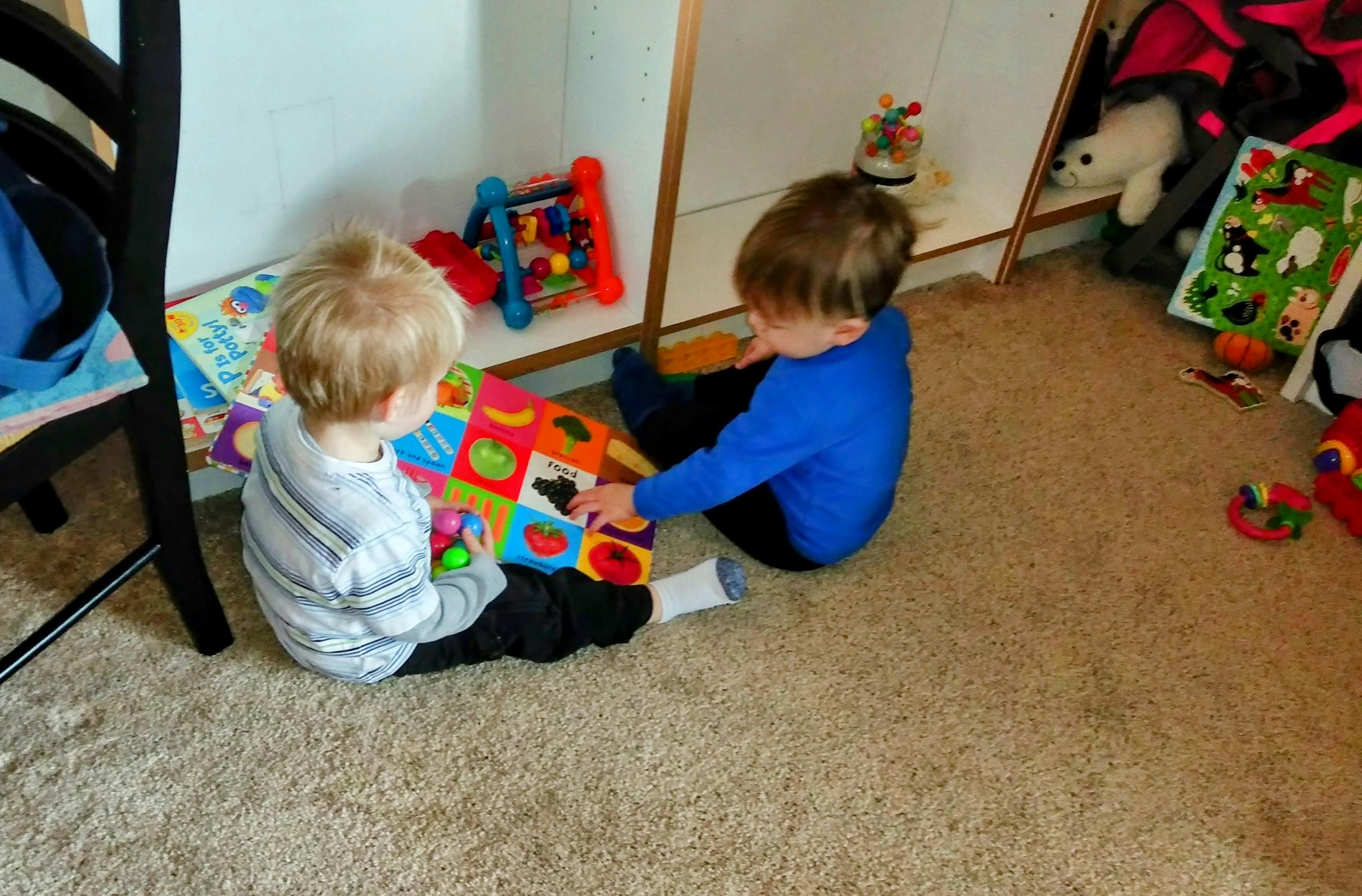 Two children sitting on a carpet playing with a colorful activity book