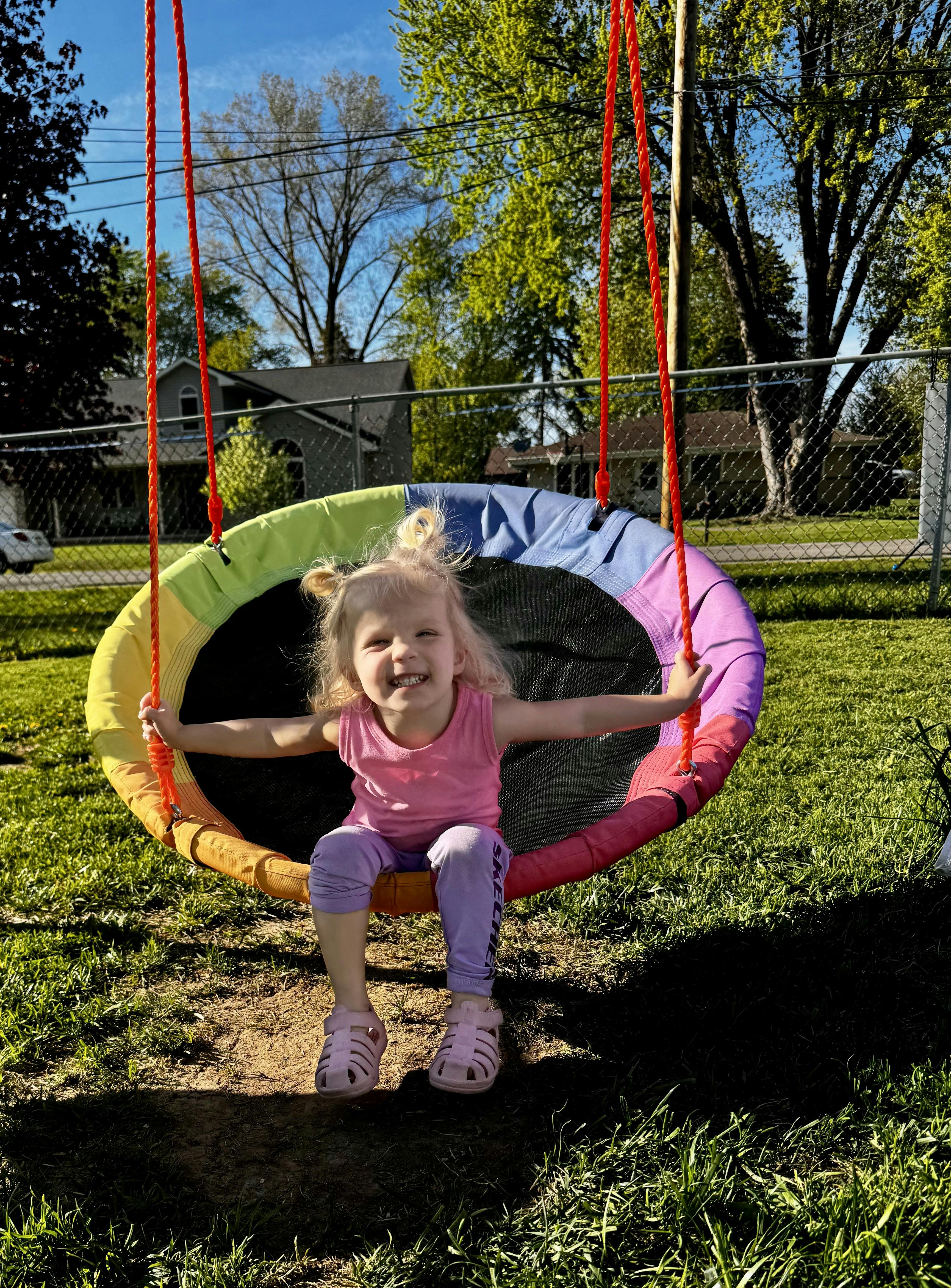 Child with pigtails sitting in a colorful round swing