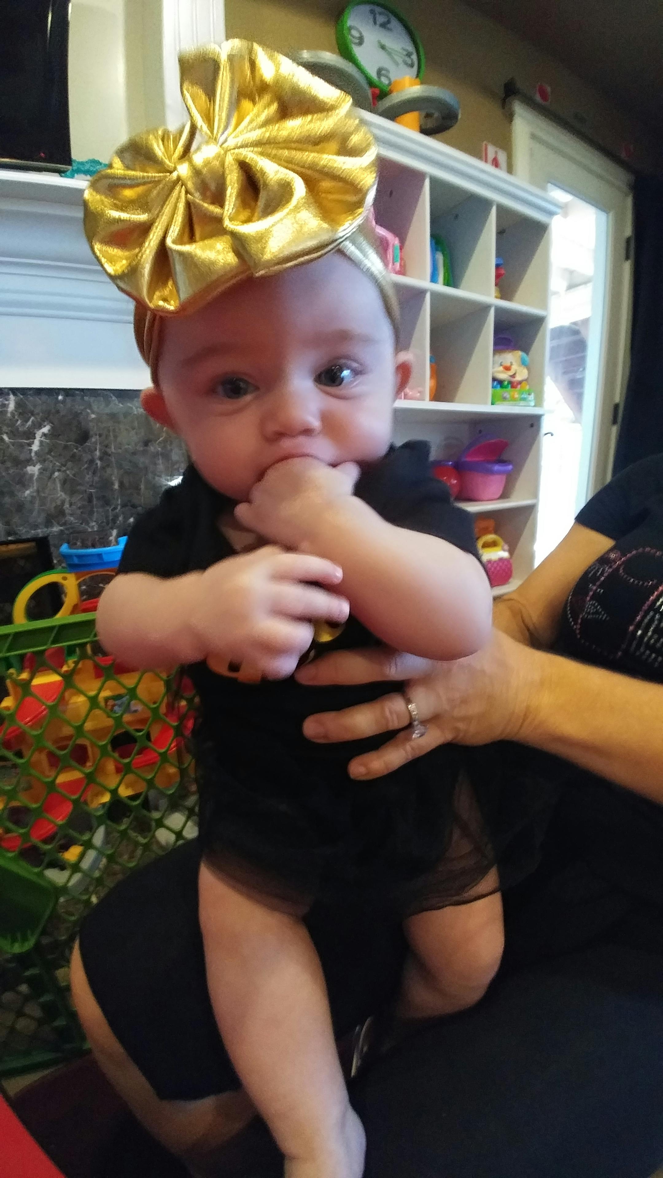 Child in a black outfit and a gold bow on their head