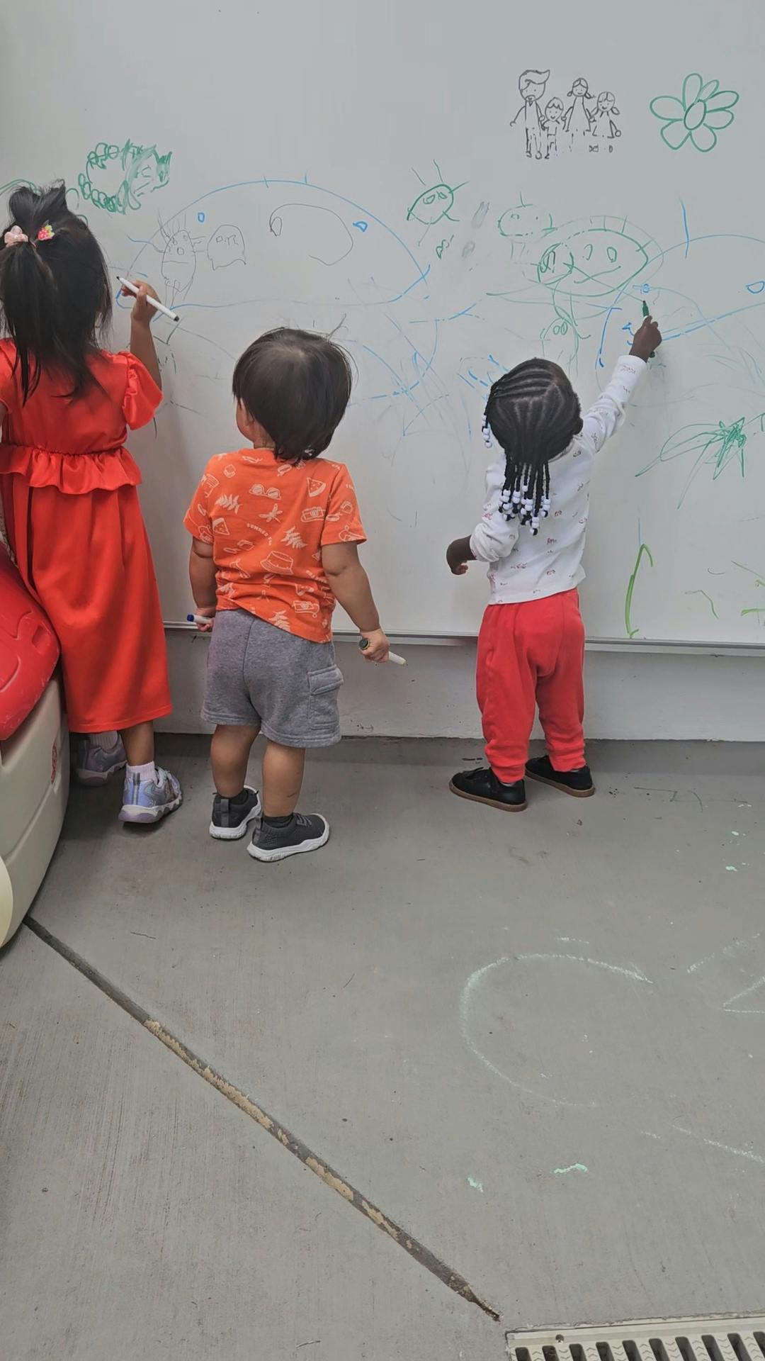Three children drawing with markers on a large whiteboard
