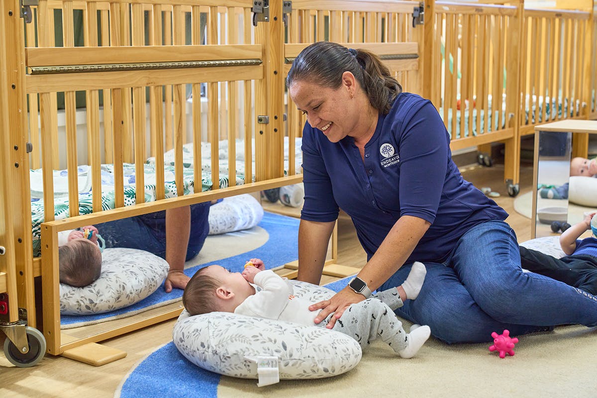 Person interacting with a child lying on a pillow on the floor