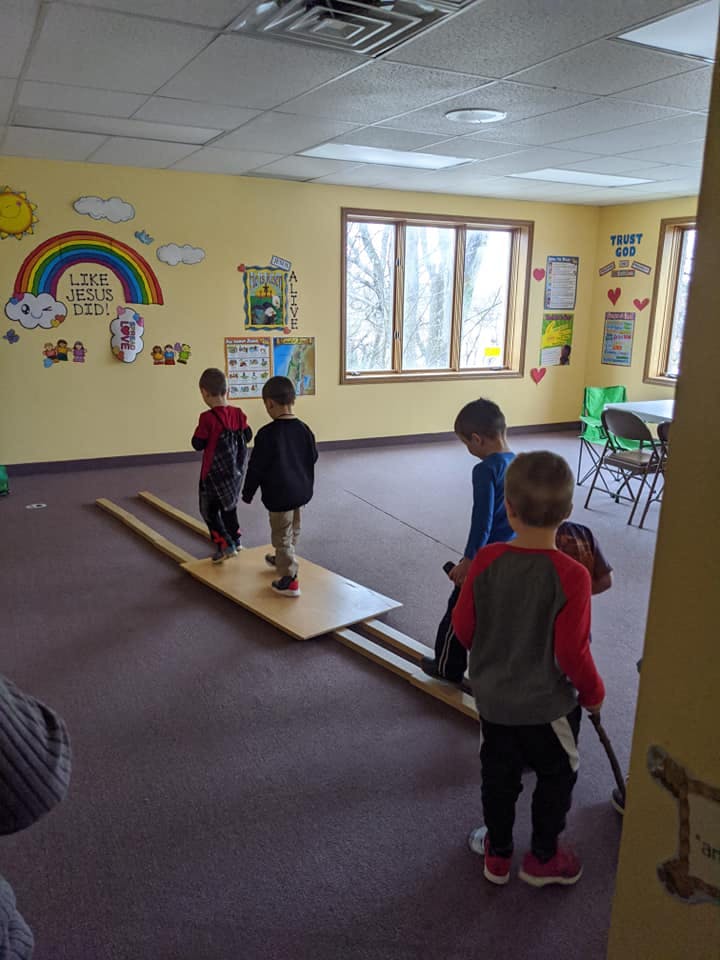 Children playing on a wooden balance beam in a room