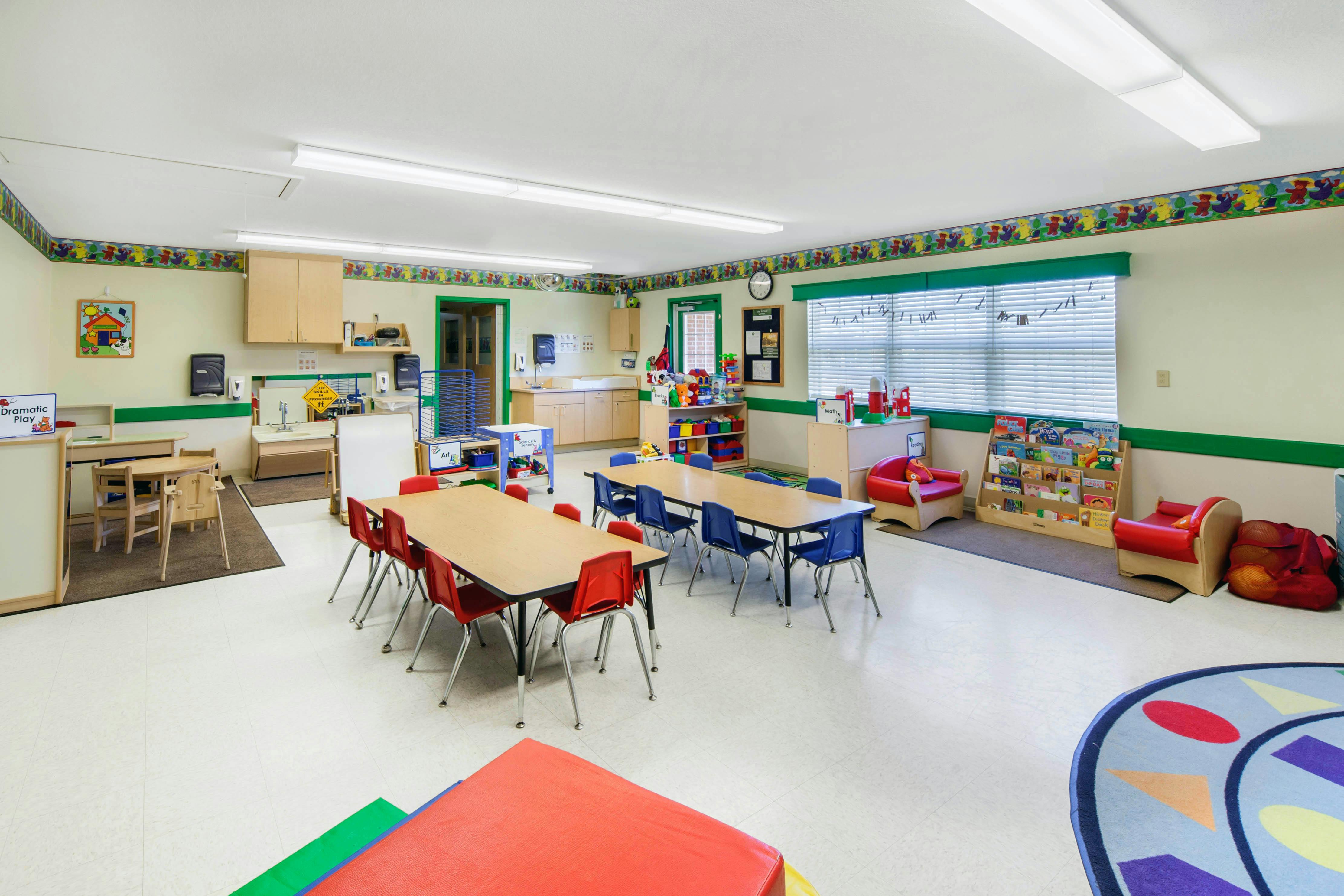 Classroom with child-sized tables and chairs, play areas, and educational materials