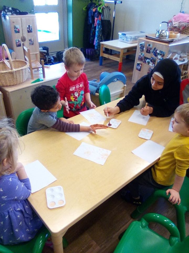 Adult and children painting at a table in a classroom