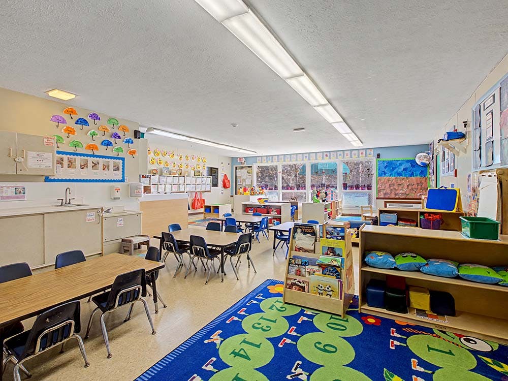 Colorful and organized classroom with small tables, chairs, bookshelves, and large windows