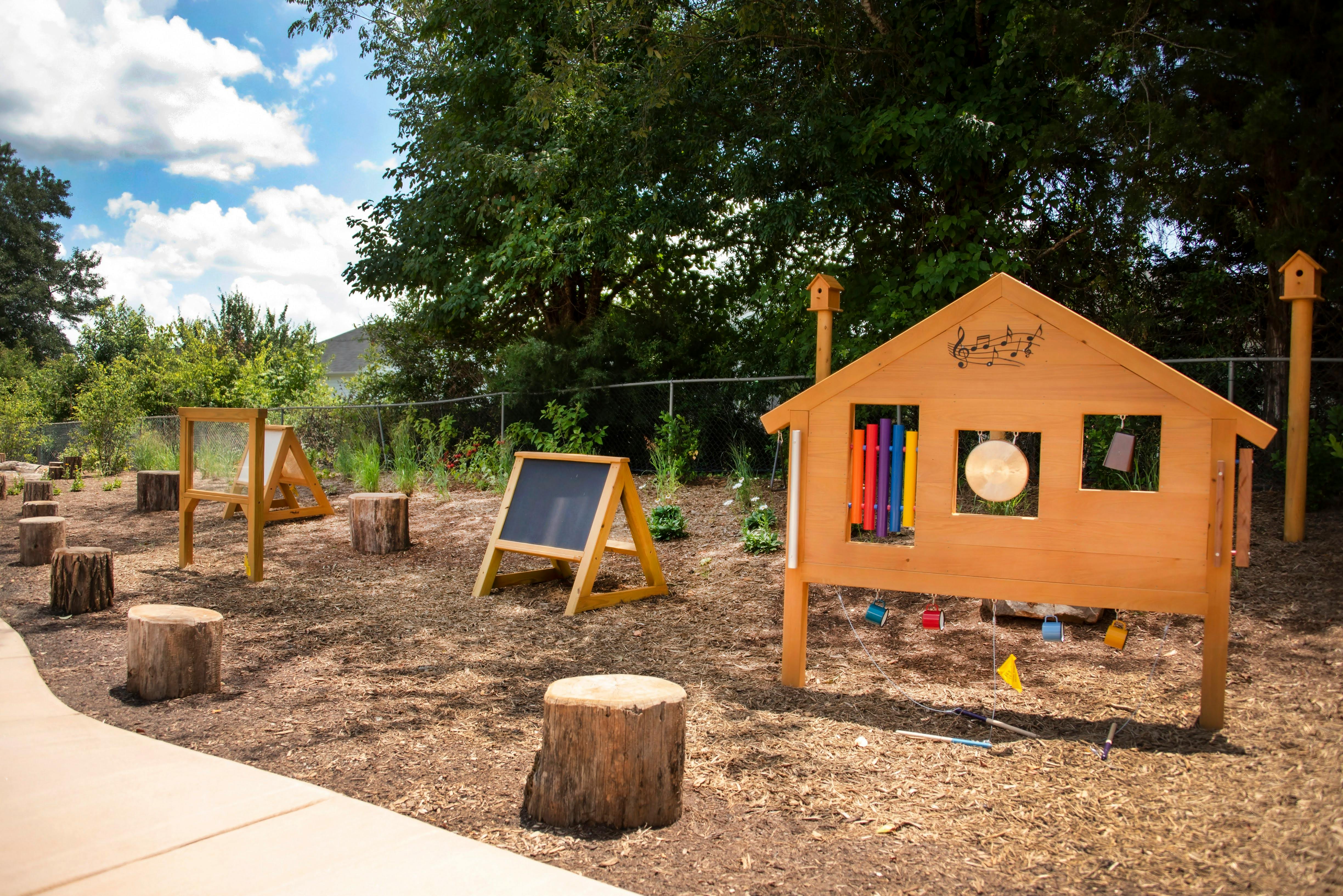 Outdoor play area with wooden playhouse, easels, and tree stump seats