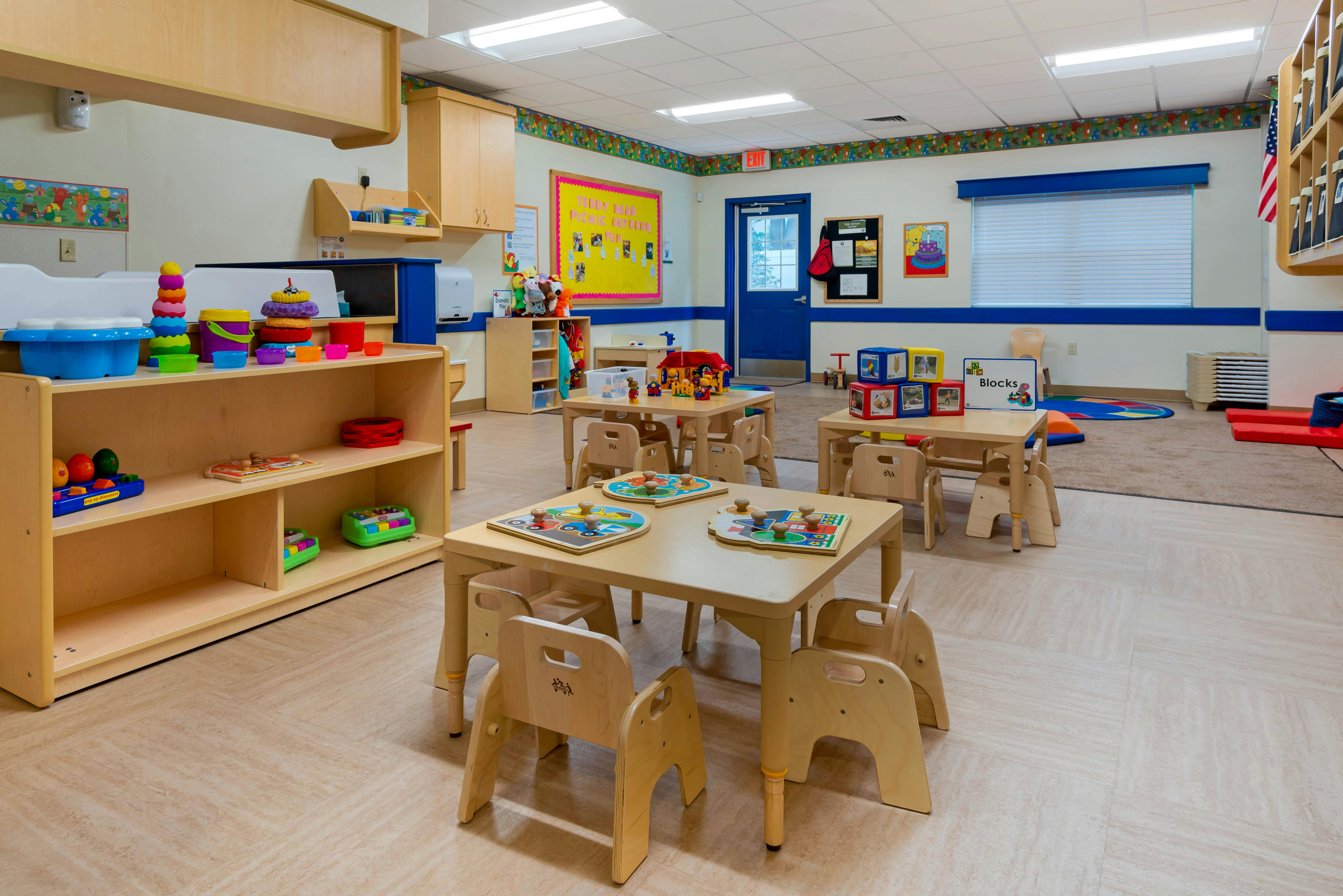 Classroom with small tables and chairs, shelves with toys, and posters on the walls