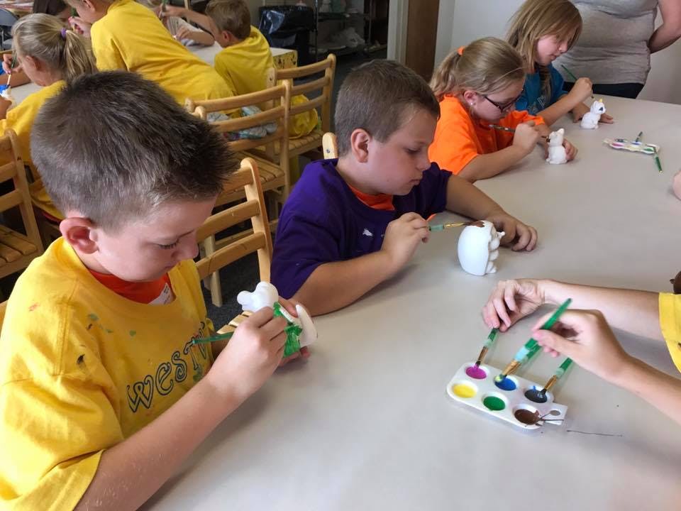 Children painting small white objects at a table