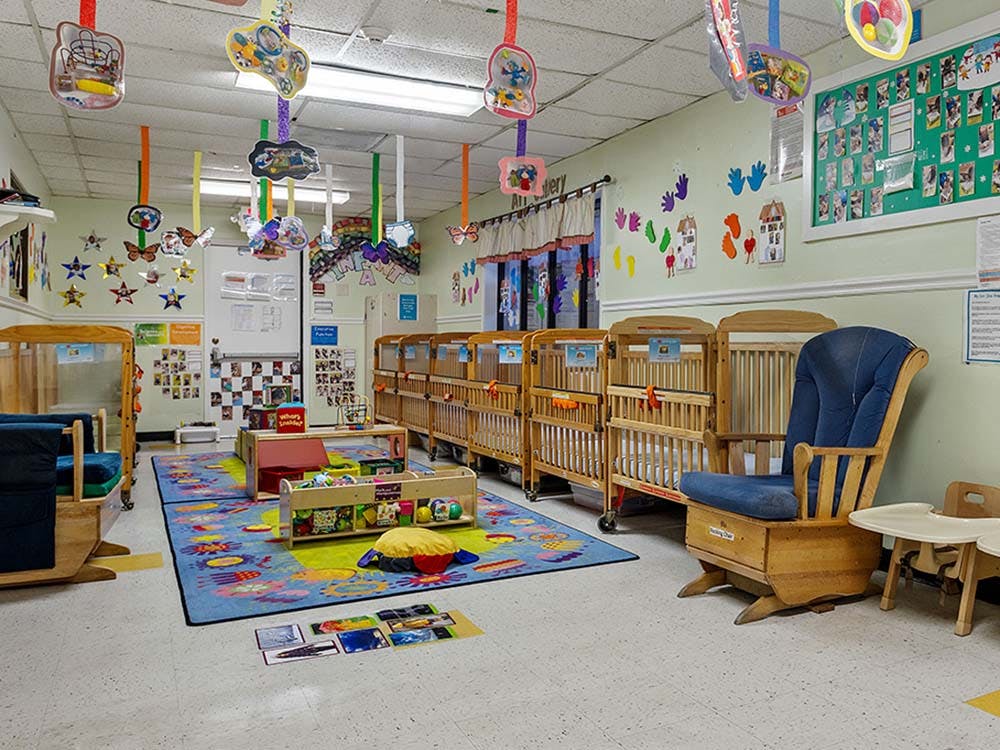cribs, a rocking chair, and a playmat in a brightly decorated room