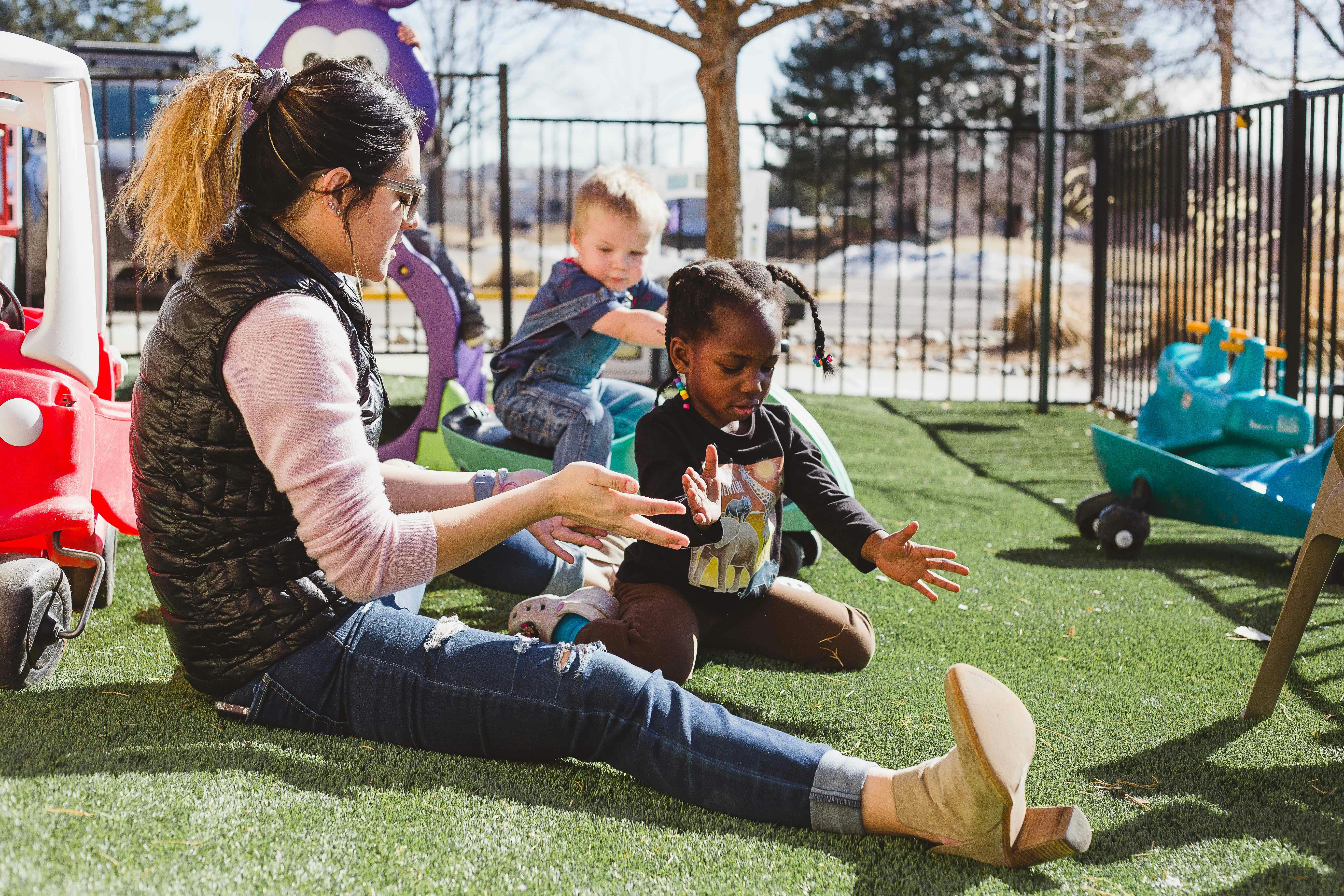 Person sitting on grass with two children playing