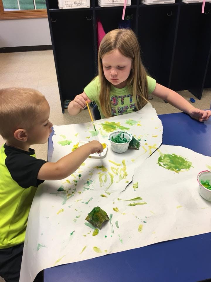 Two children painting on paper at a table
