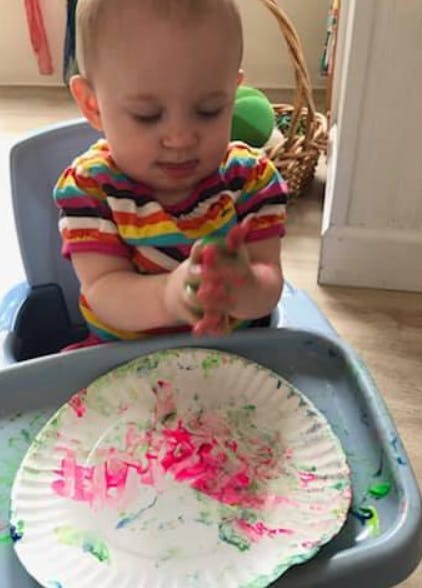 Child in high chair with paint on hands and paper plate