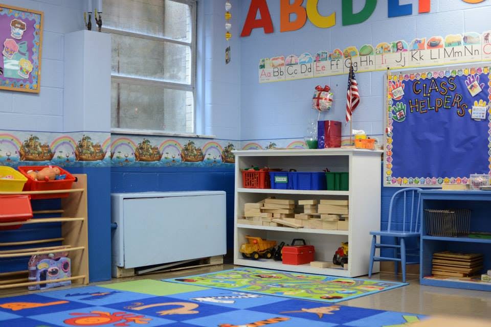 A classroom with colorful rugs, shelves with toys, and alphabet decorations