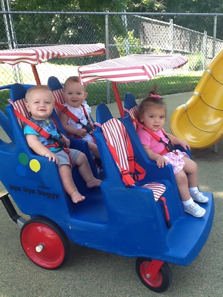 Three children sitting in a blue multi-seat stroller with striped canopies