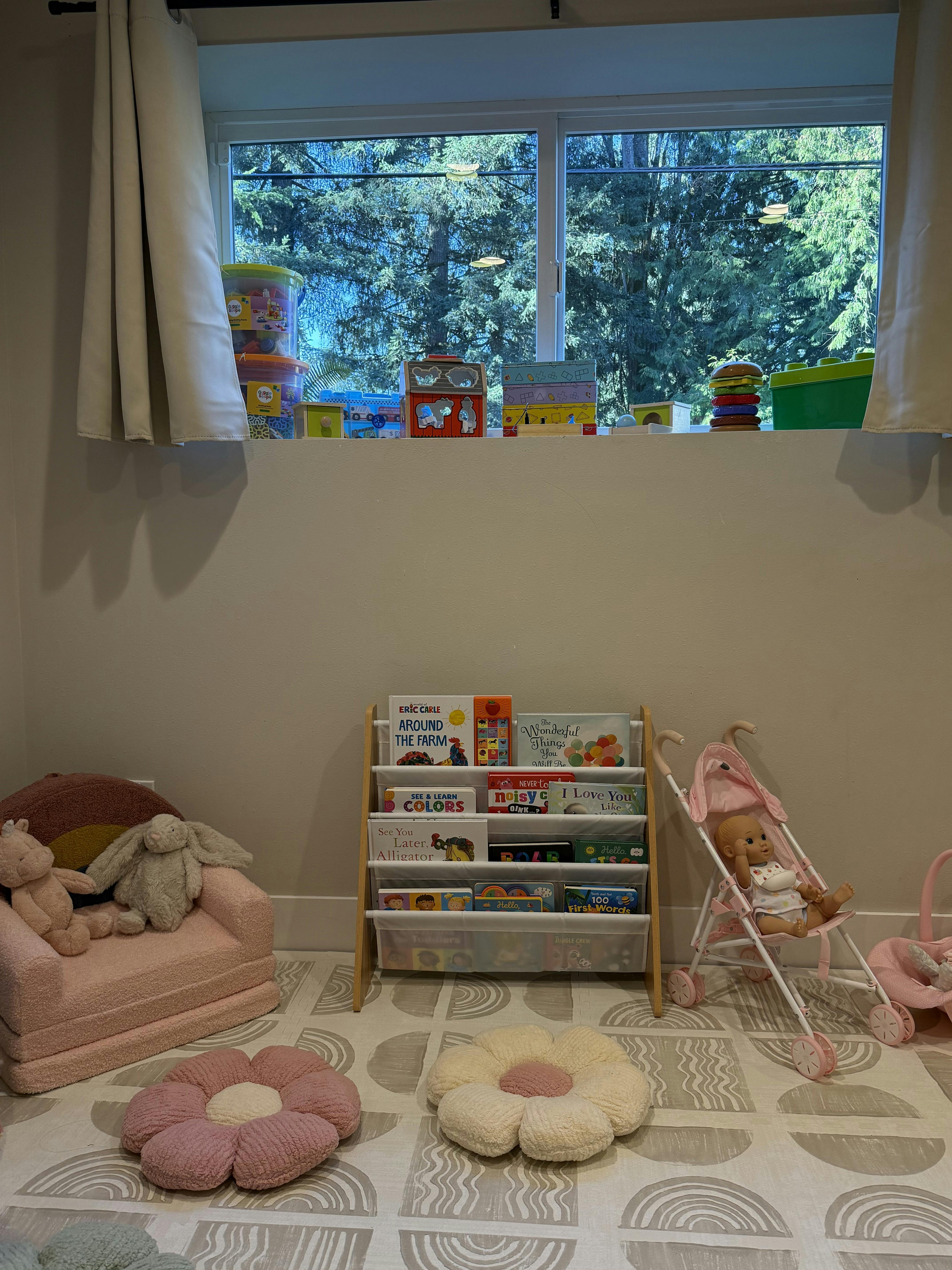 Child's play area with a bookshelf, stuffed animals in a pink chair, and flower pillows