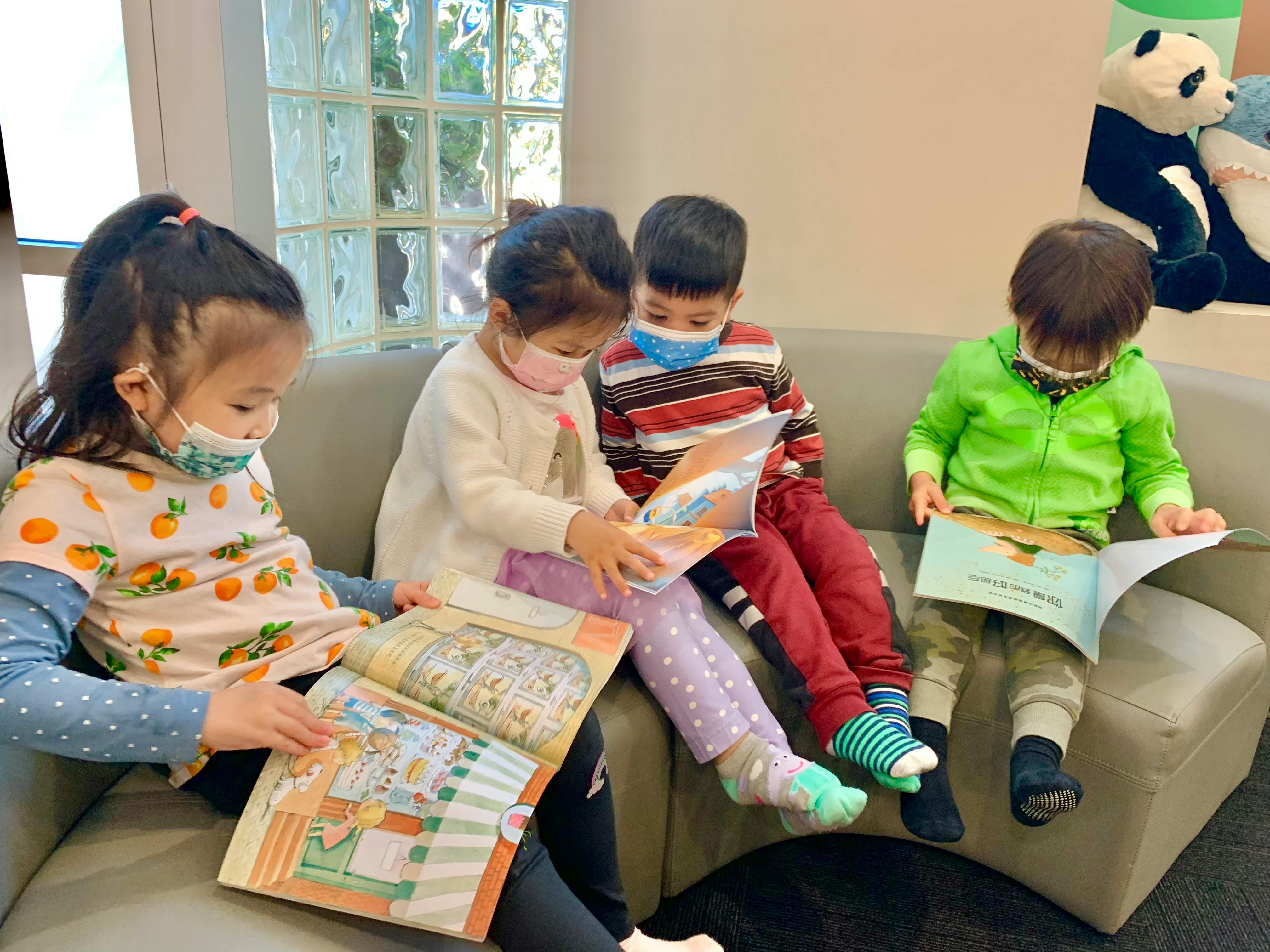 Four children wearing masks reading books on a couch