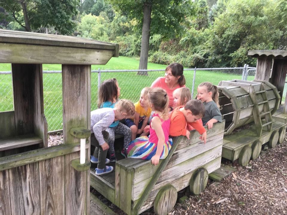 Adult and children playing on a wooden train structure outdoors